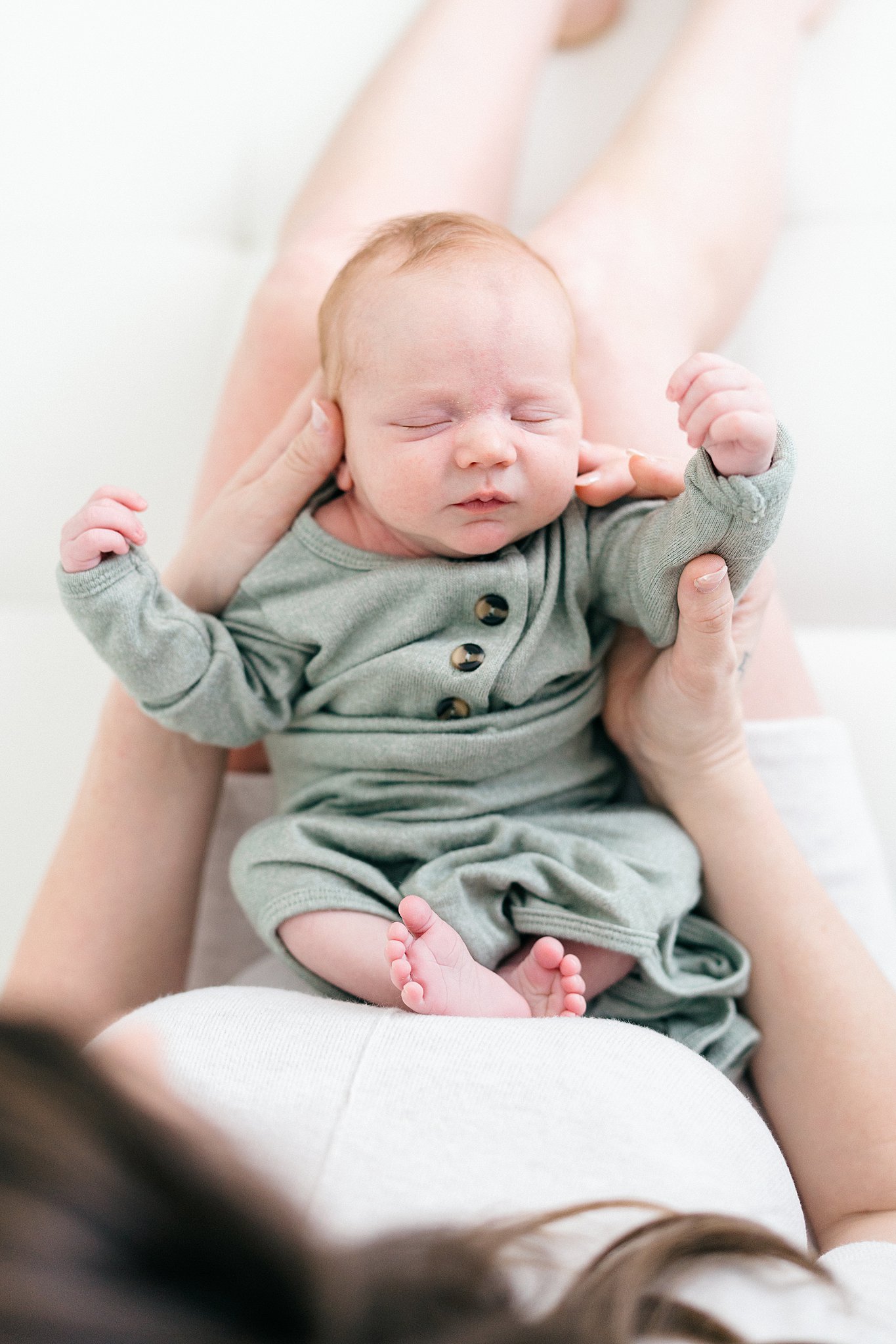 A newborn baby sleeps in a green onesie in mom's lap after visiting atlanta baby boutiques