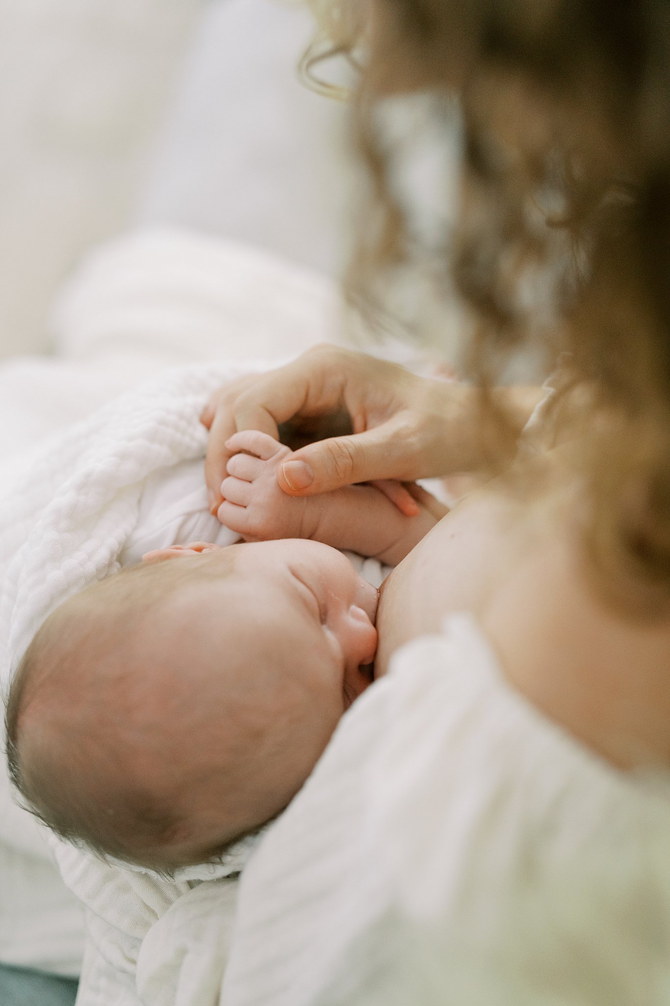 A newborn breastfeeds while mom sits in a white dress after visiting atlanta lactation consultants