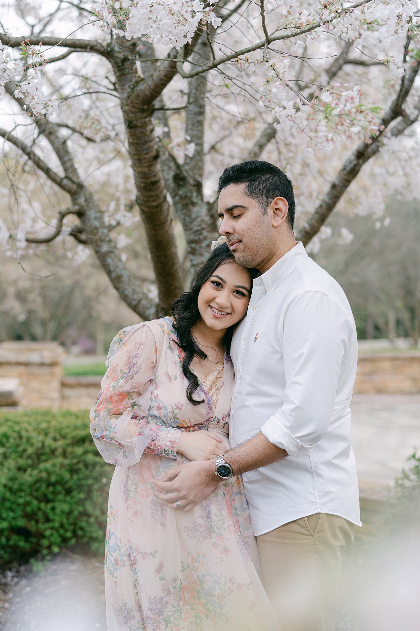 A happy expecting couple snuggles under a white blossoming tree in a park after meeting atlanta midwives