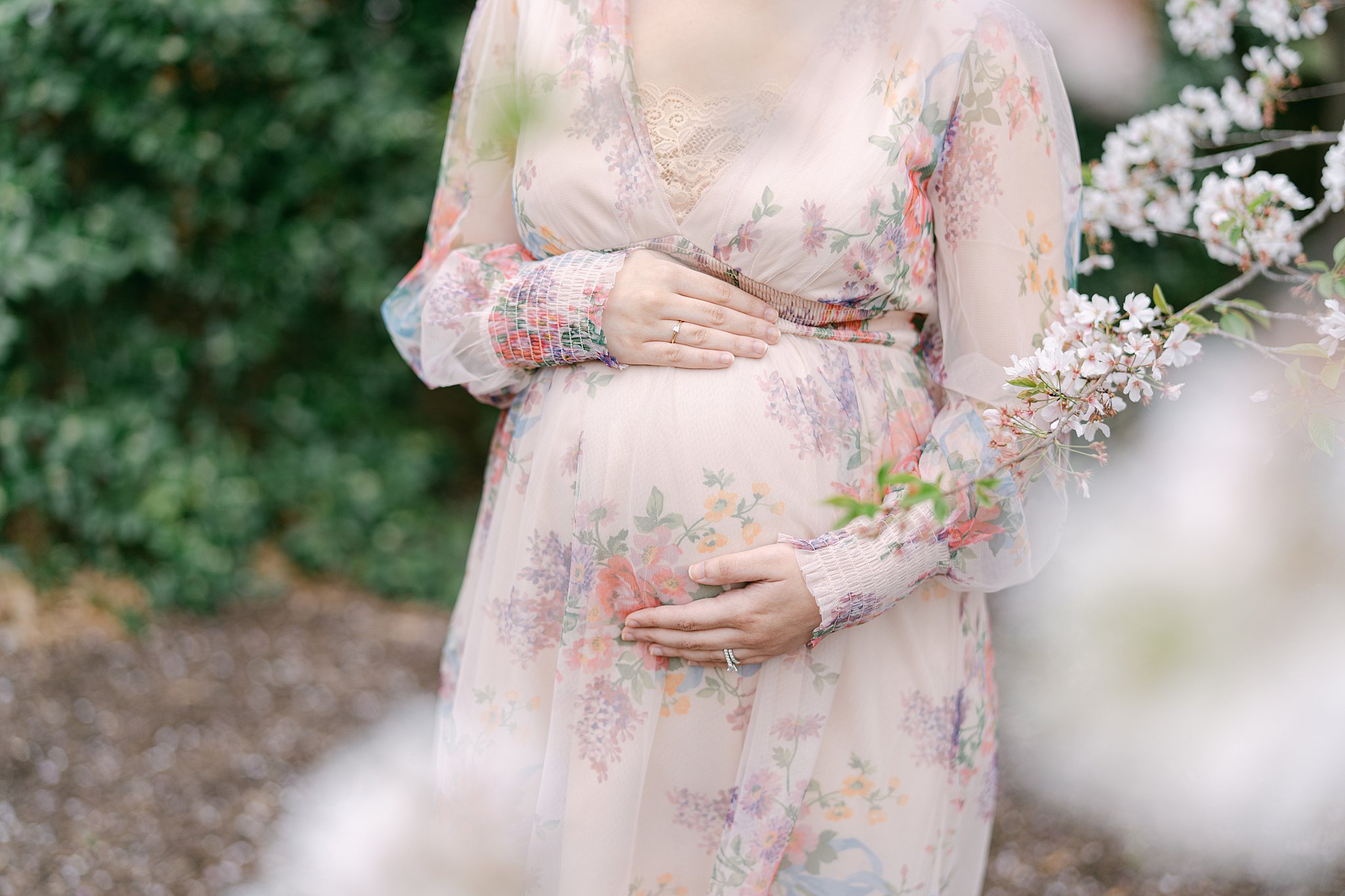 Details of a mom to be holding her bump in a garden in a pink floral print dress after meeting atlanta midwives