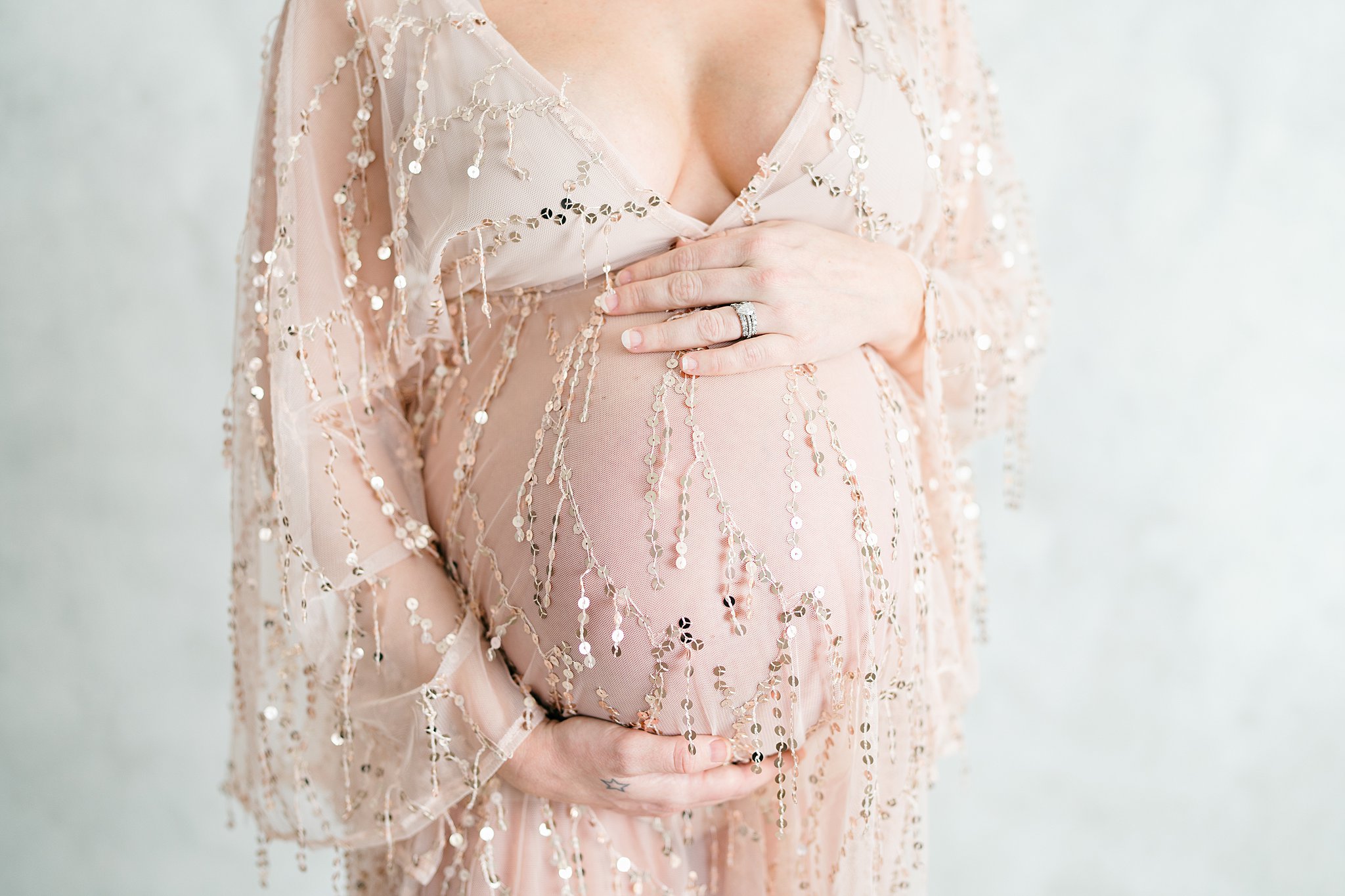 Details of a mother to be standing in a gold maternity gown with hands on her bump after visiting baby shower venues in Atlanta