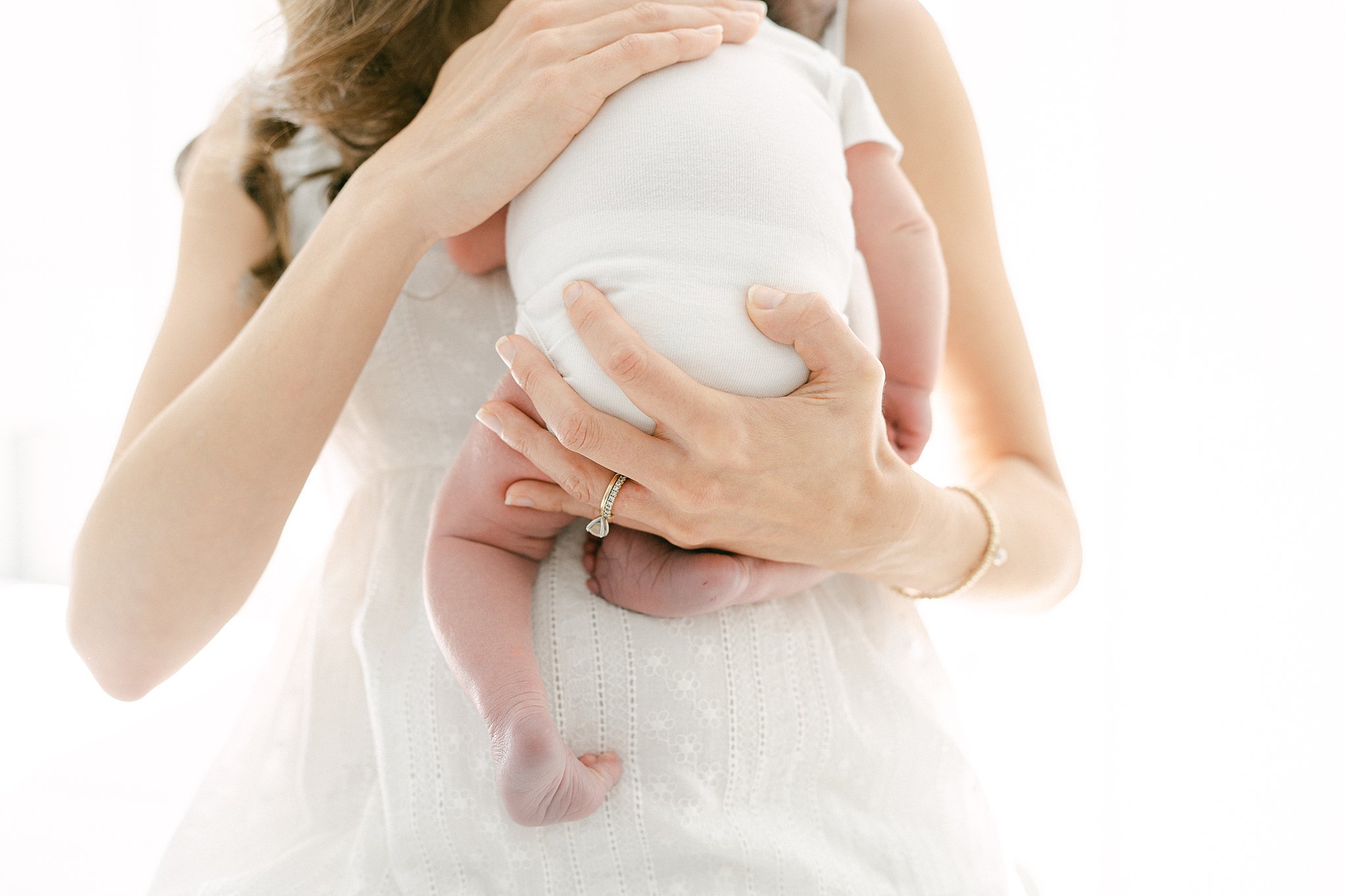 Details of a mom's hand on her newborn while holding it against her chest