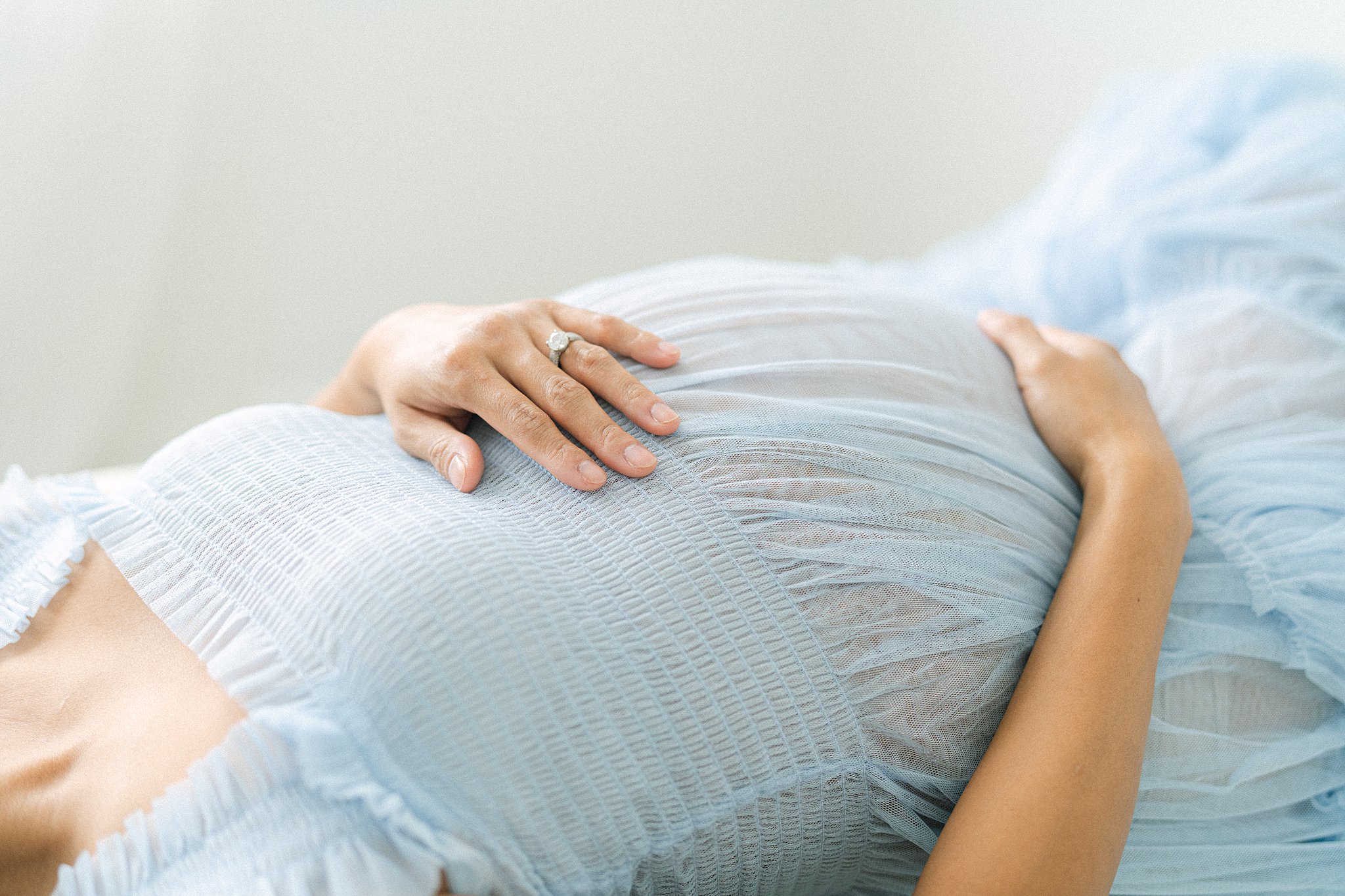 Details of a mom to be laying in a blue maternity gown with hands on bump after a prenatal massage in Atlanta